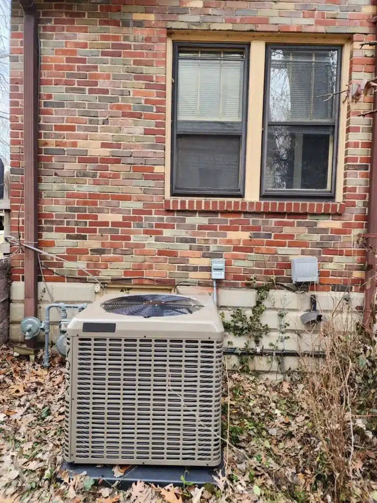 A beige air conditioner located in the back of a red brick house